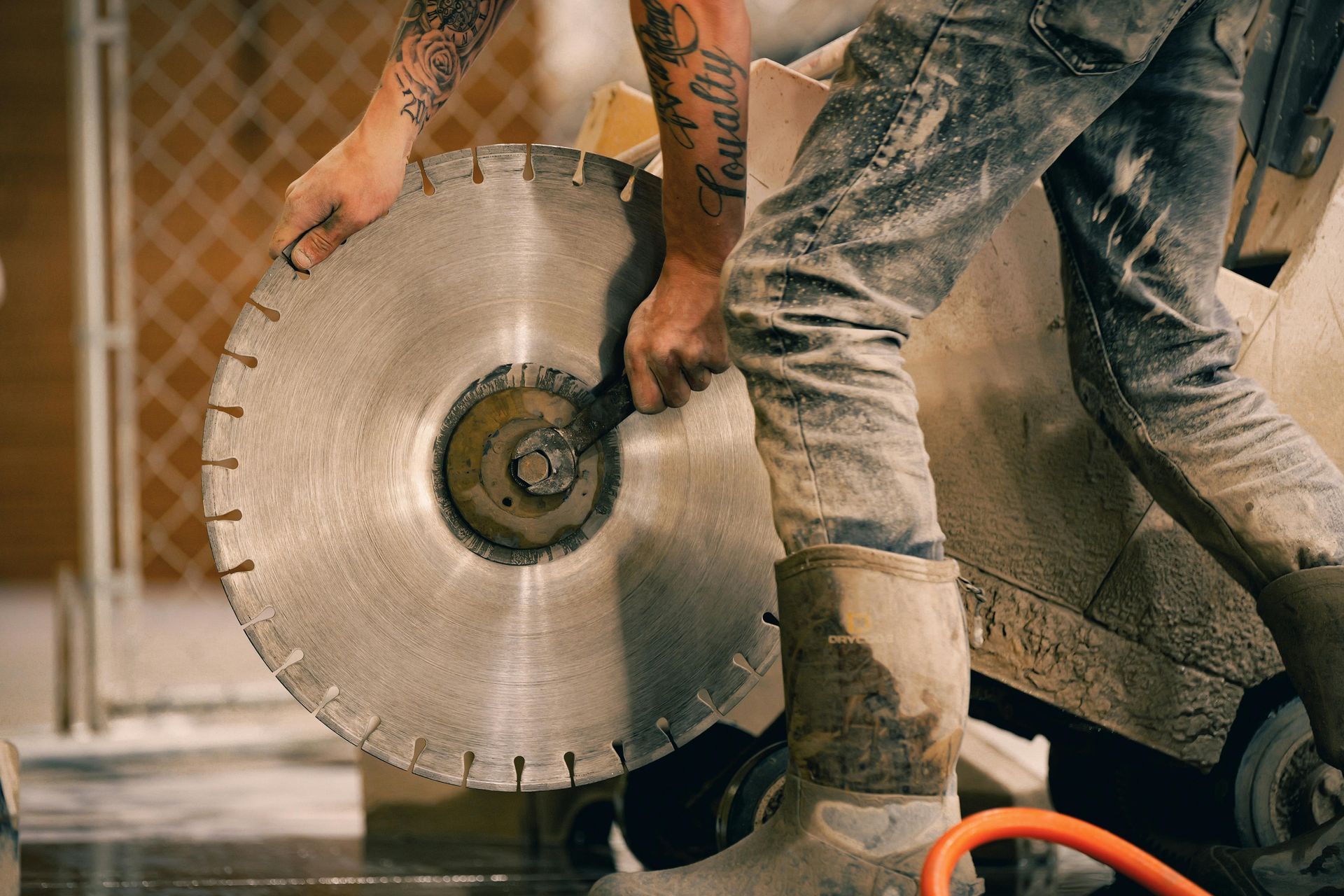 Worker handling a large circular saw blade at a construction site, covered in dust and debris