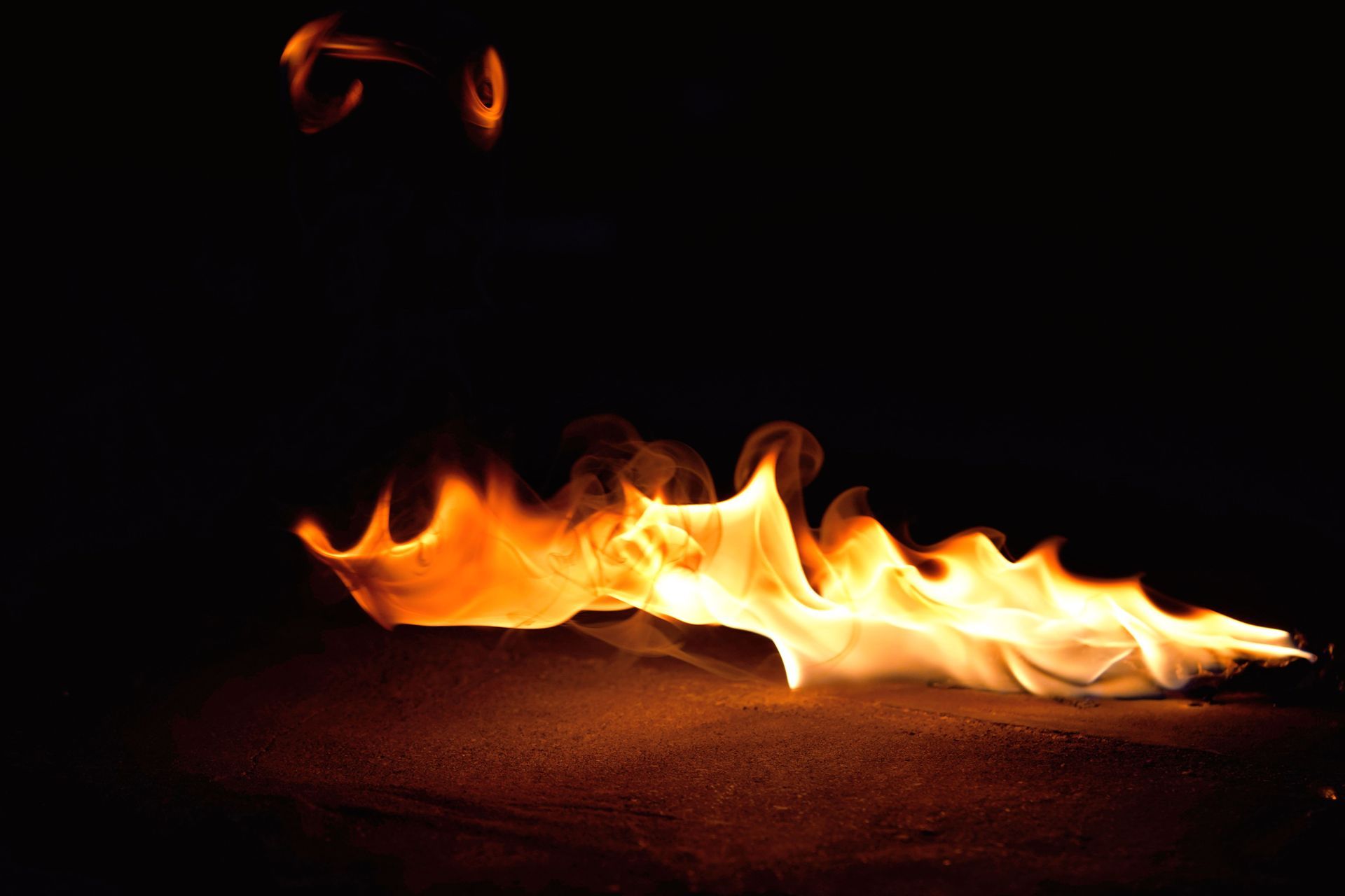 Small orange flames flicker across a dark floor in a black background.