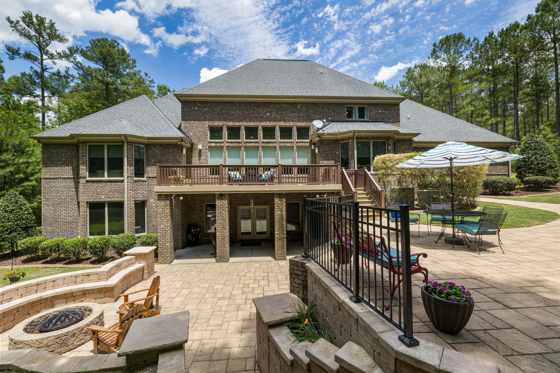 Large brick house with a stone patio, outdoor seating, stairs, and a pool area under a blue sky