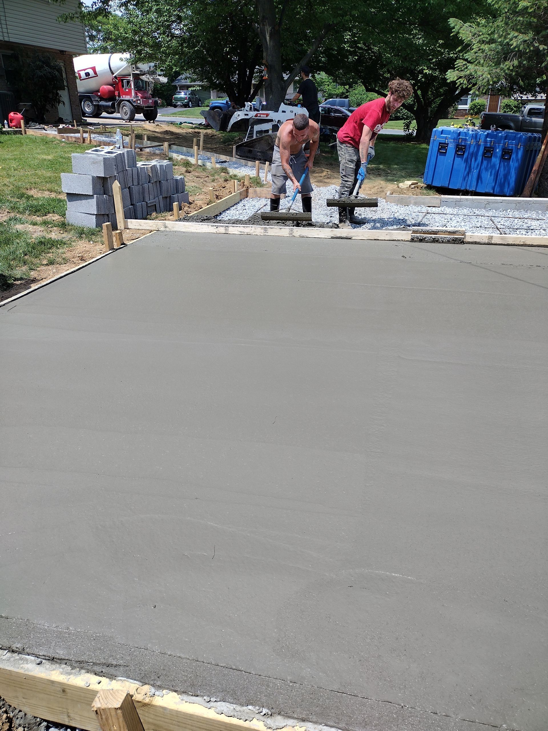 Two workers smooth freshly poured wet concrete into a level surface at a residential driveway construction site.
