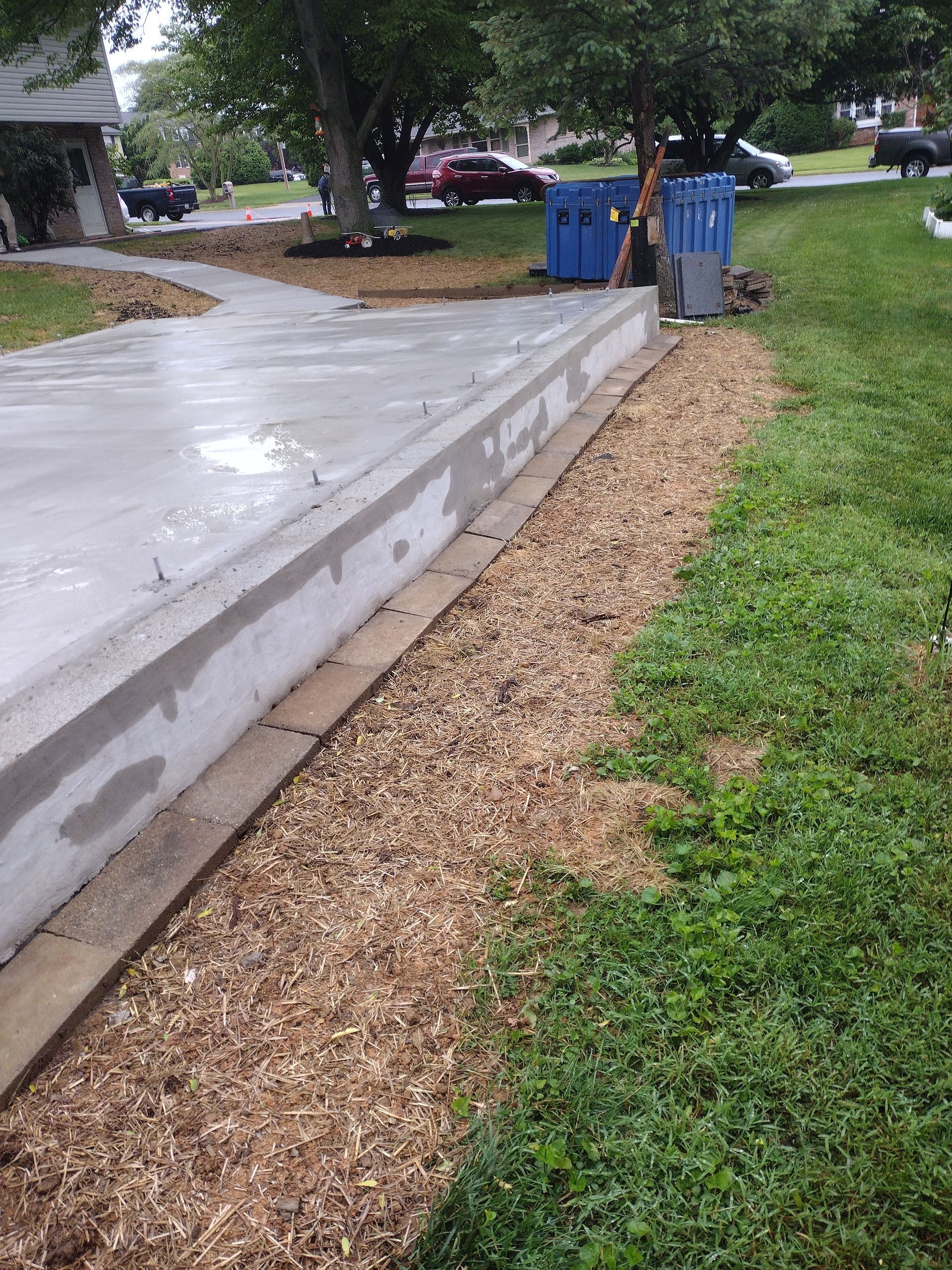 Freshly poured concrete slab with wooden formwork bordering a mulched garden bed in a residential yard.