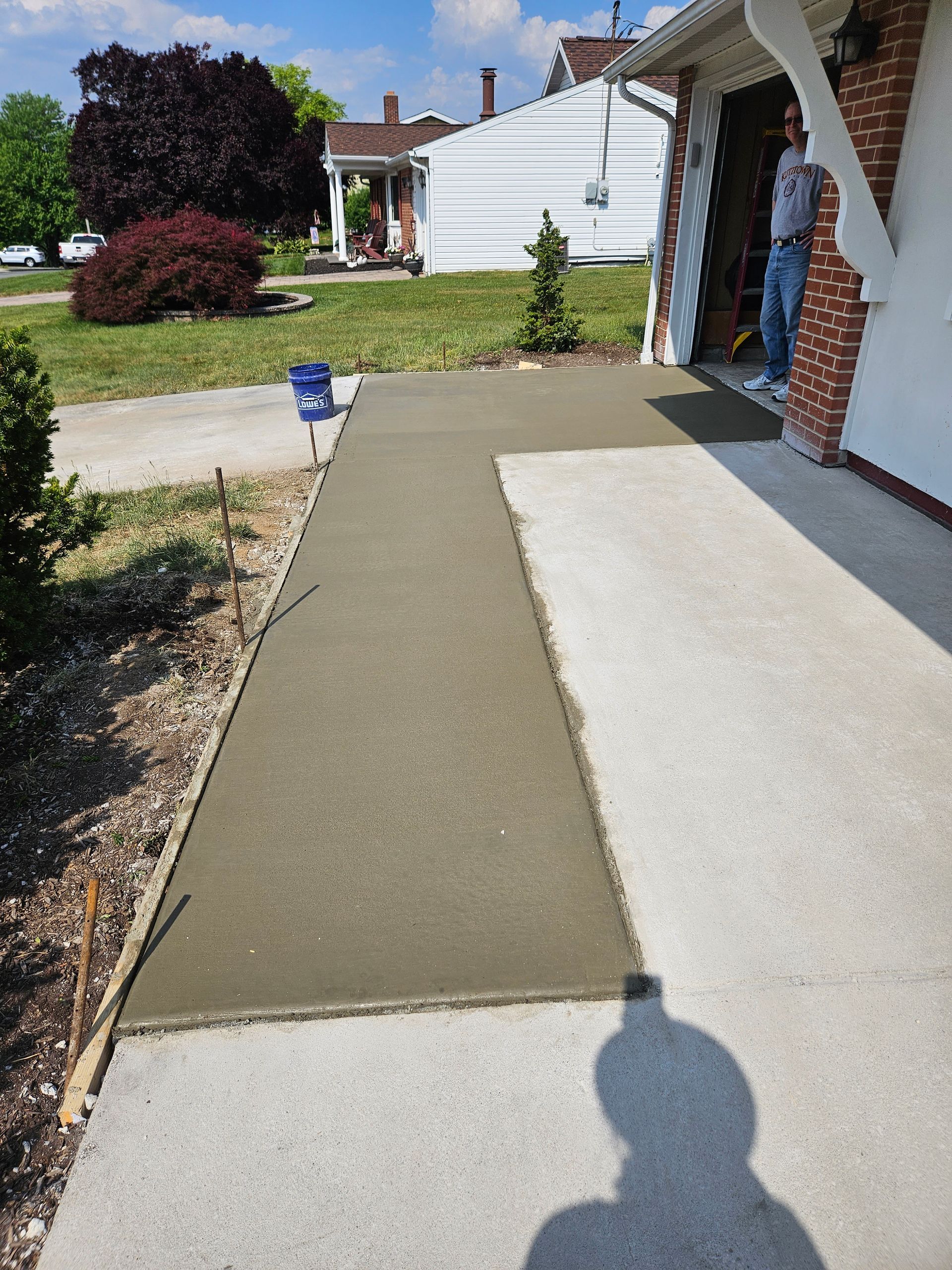 A freshly poured concrete sidewalk extension next to an existing walkway leading to a house entrance.
