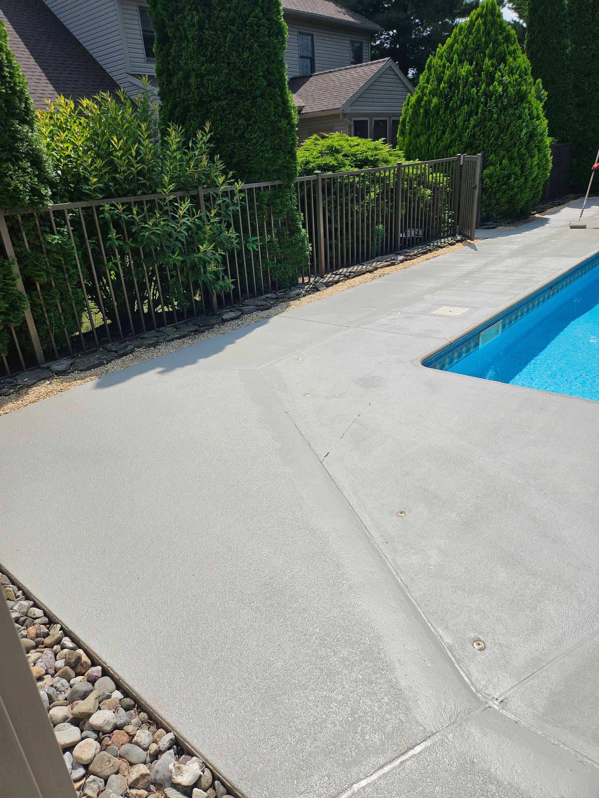 A concrete pool deck with a visible diagonal crack leading to the edge of a swimming pool near a residential home.