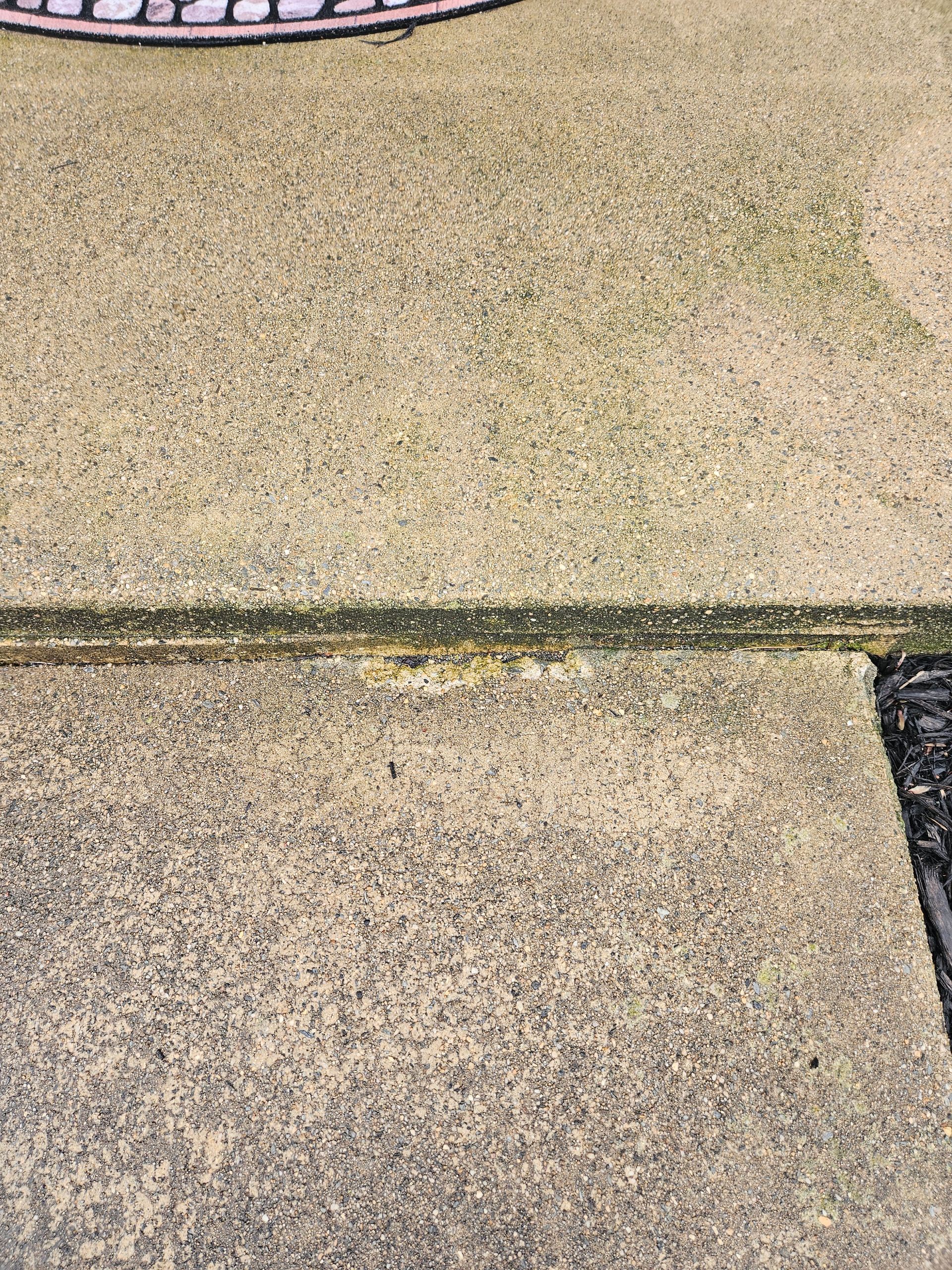A close-up of a damaged concrete slab joint with a small triangular piece of cement missing at the edge.