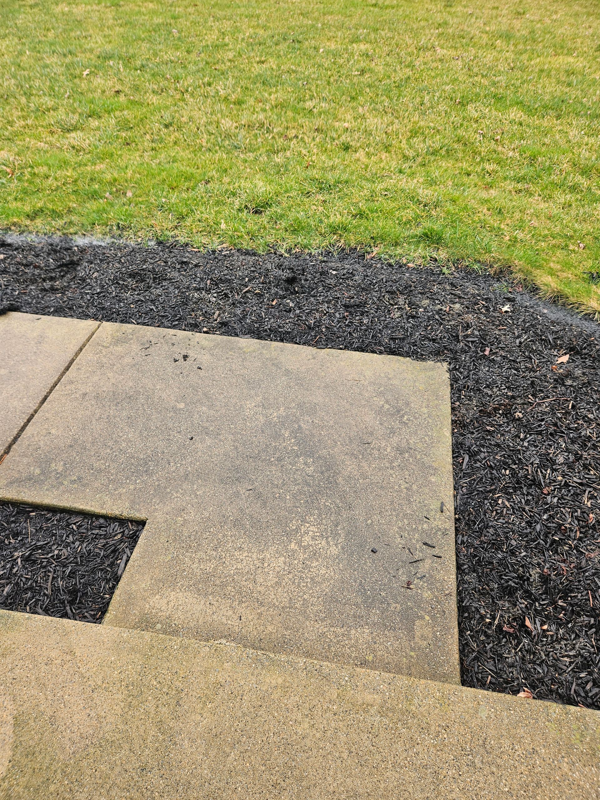 Tan concrete pavers meet a bed of dark gravel mulch beside a green grass lawn.