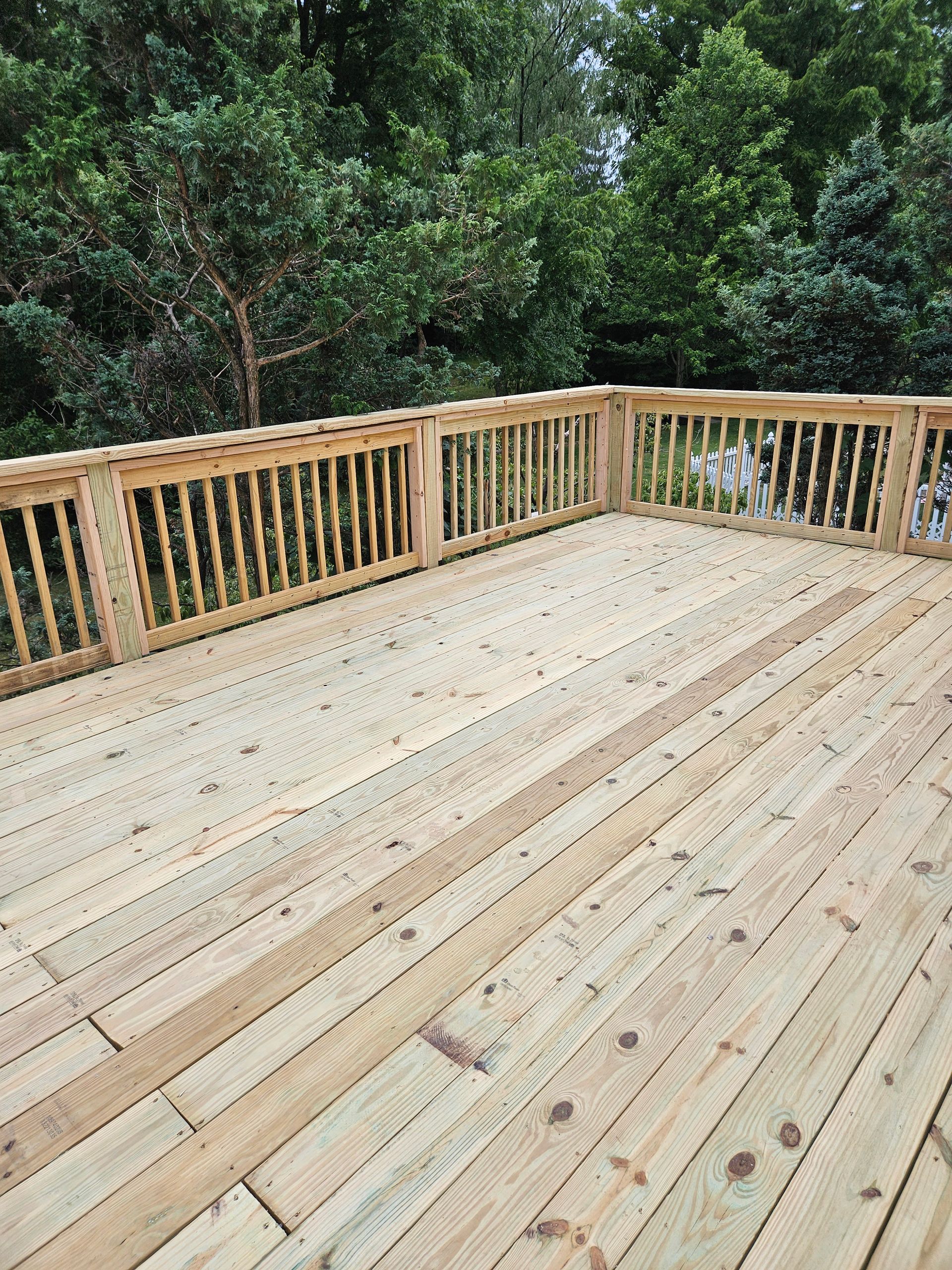 A high-angle shot of a clean, light-colored wooden deck with simple railings overlooking lush green trees.