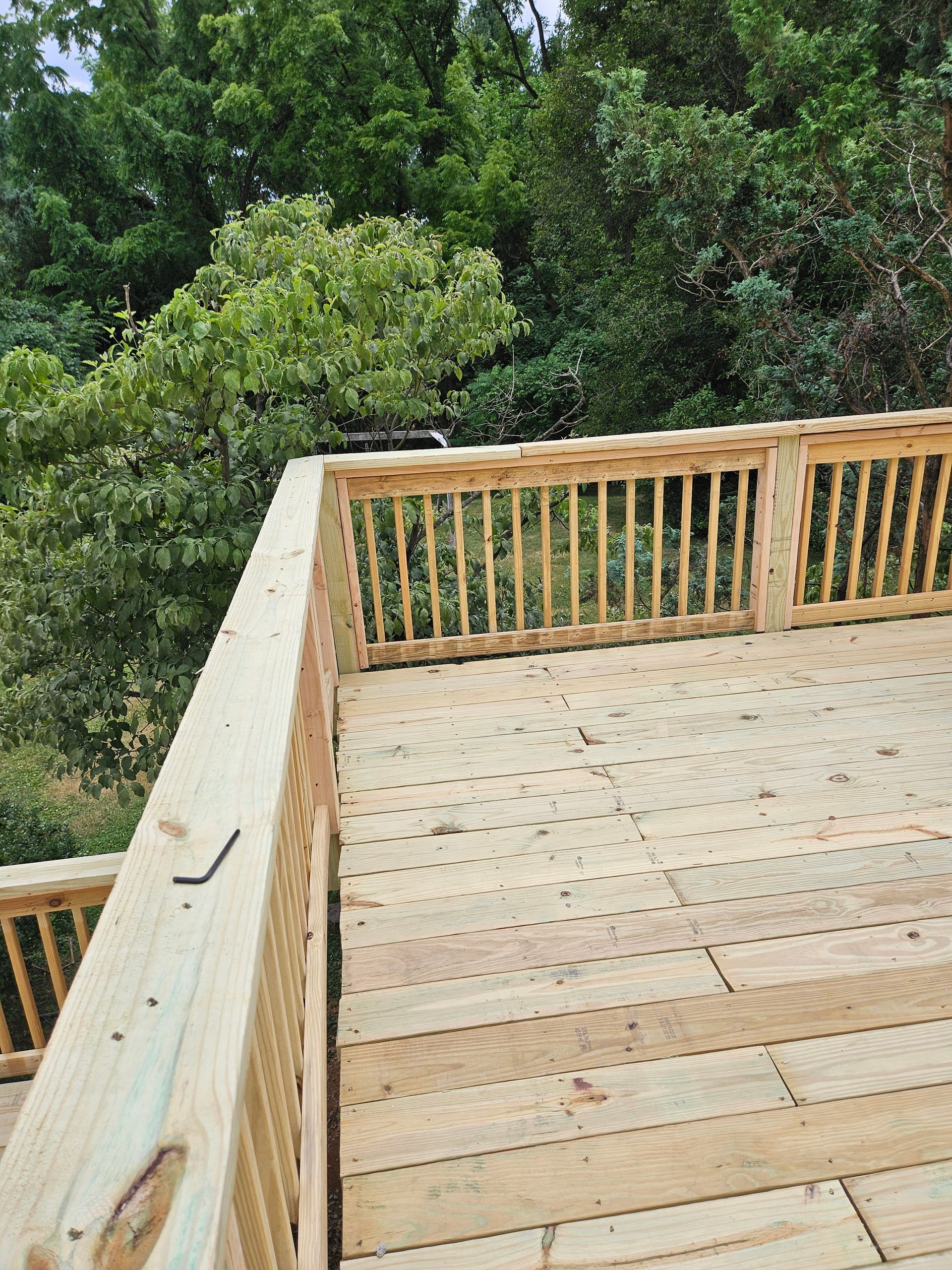 A high-angle view of a partially constructed wooden deck with railings, set against a backdrop of trees.
