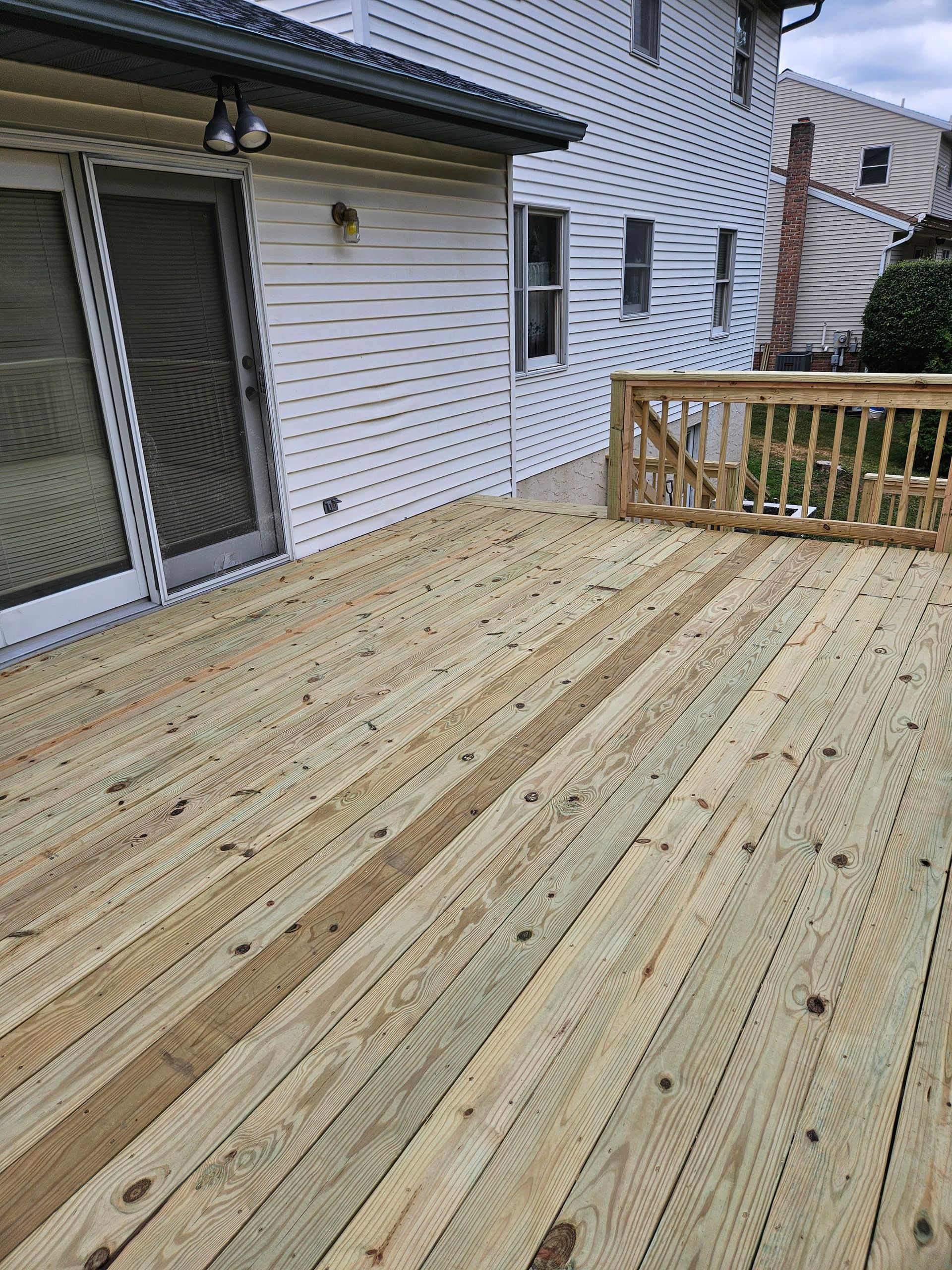 A newly built wooden deck attached to a white-sided house with a sliding glass door and a wooden railing.
