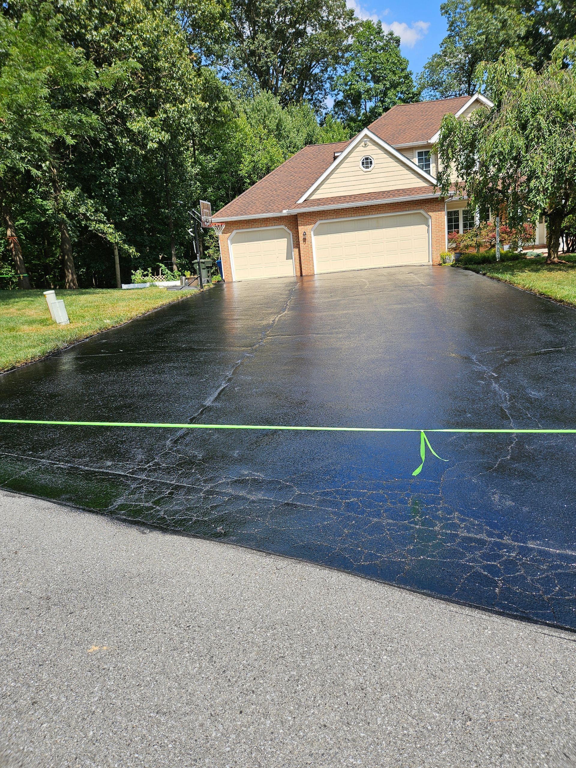 A freshly seal-coated, dark black driveway leading to a house with a two-car garage, blocked by a thin green cord.