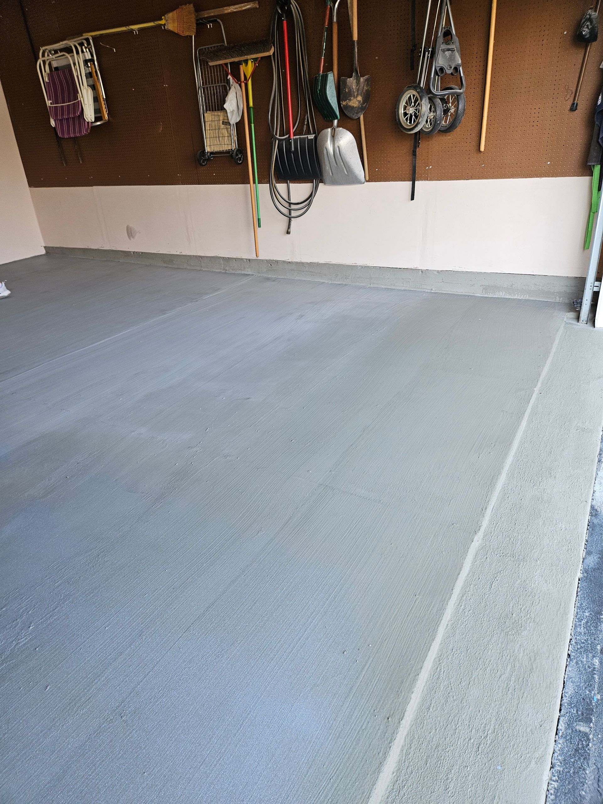 A view of a garage interior with a gray coated concrete floor and various tools hanging on a pegboard wall.