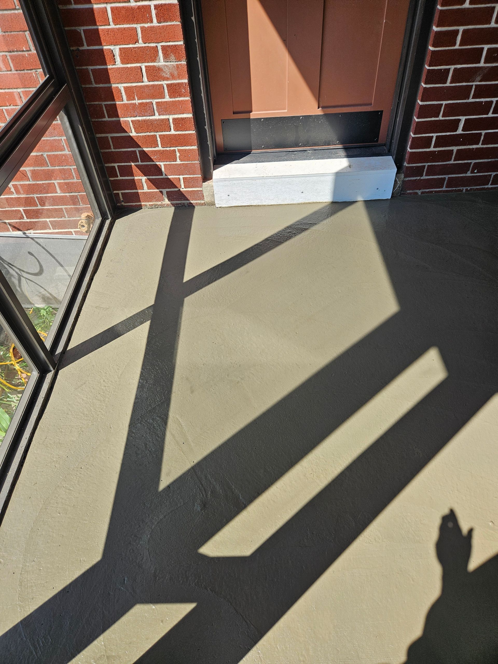 A concrete porch with a white threshold at a brick doorway, showing long shadows cast by the porch screening.