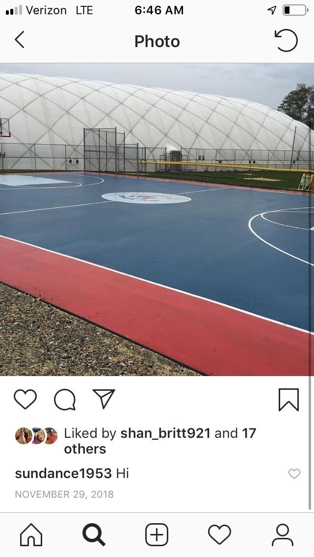 A blue basketball court with red borders located outdoors in front of a large, white, arched fabric structure.