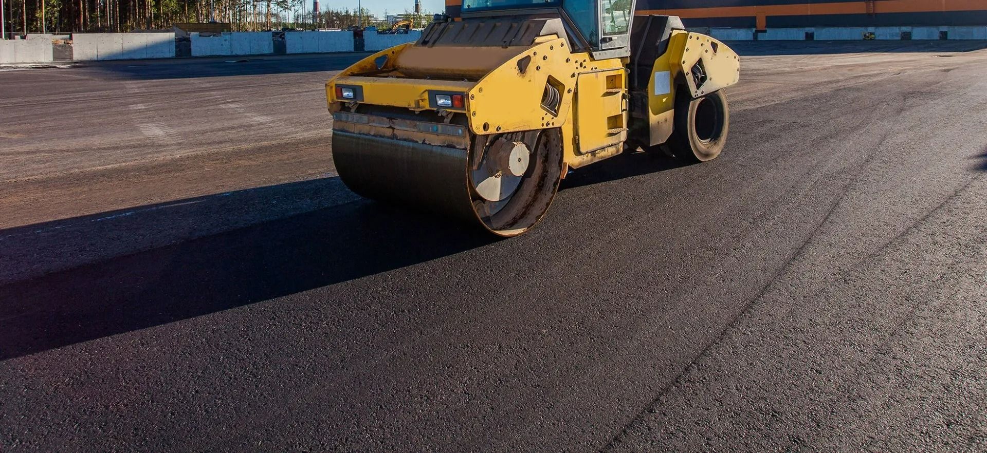 Yellow road roller compacting fresh asphalt on a street at sunset