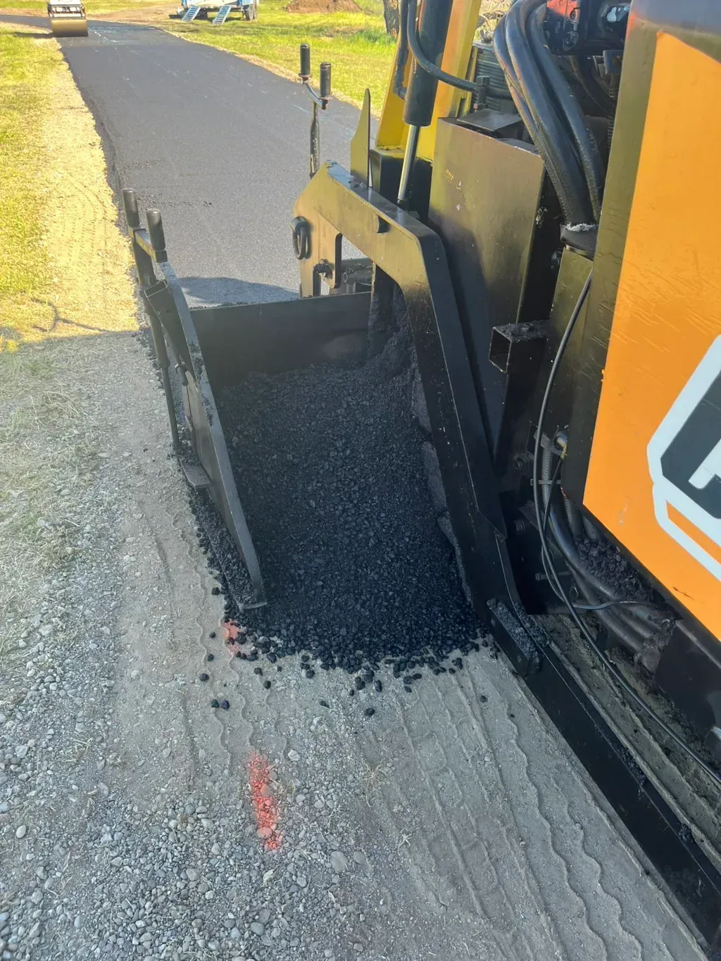Road paving machine spreading black asphalt on a paved roadside shoulder