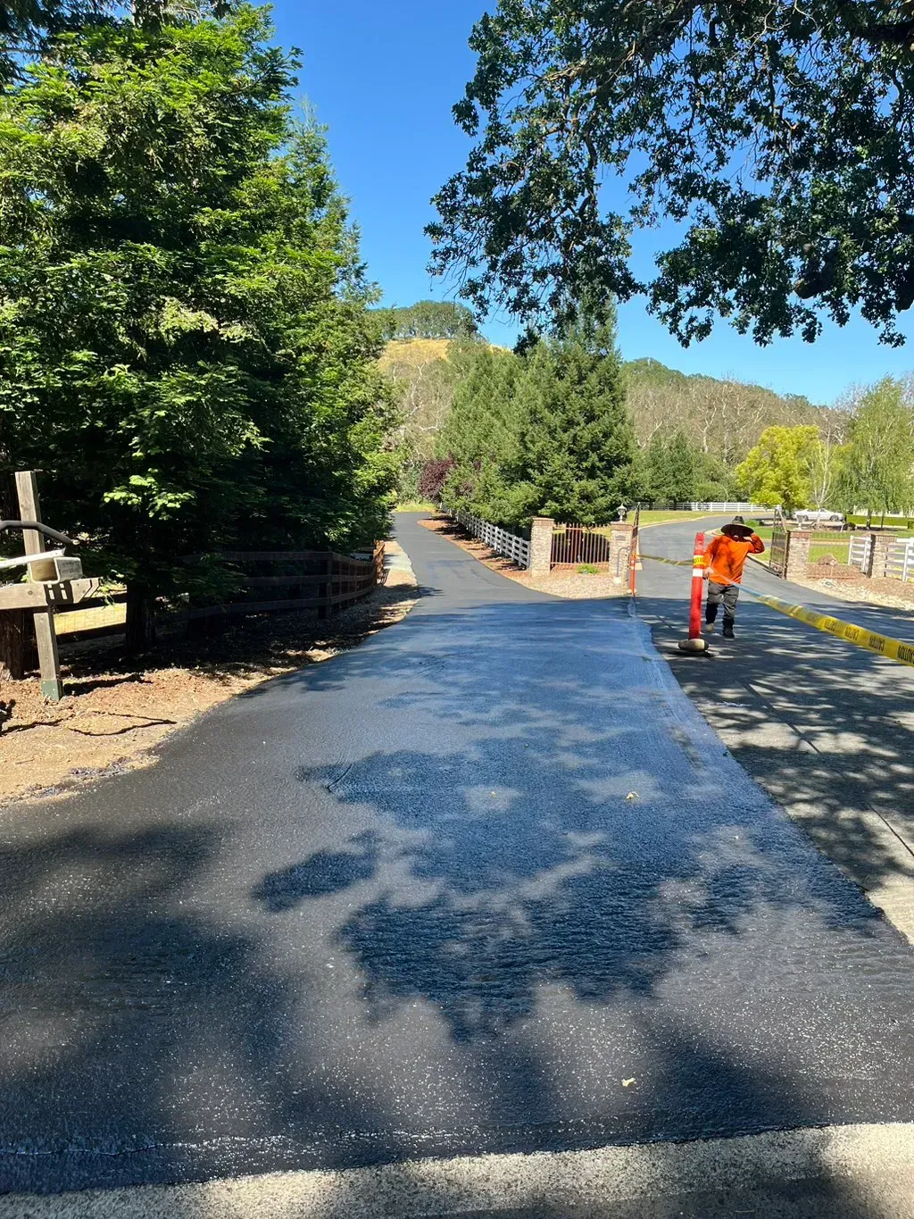 Paved trail through trees and stone walls, with a worker in orange cones on the right.