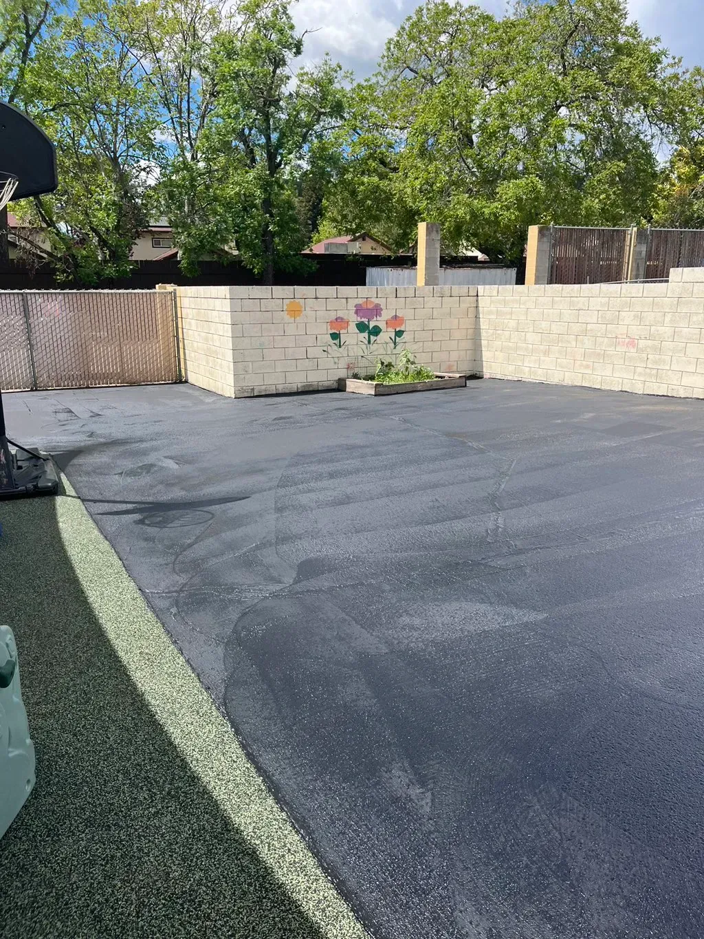 Empty paved backyard with a low stone wall, trees, and a mural in the background.