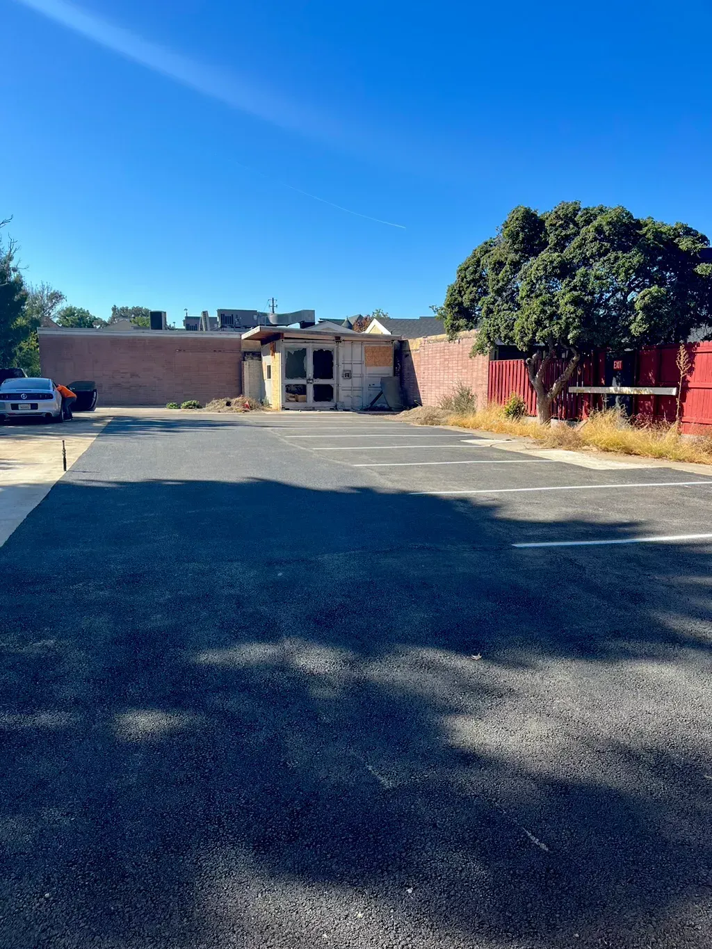 Empty parking lot with a brick building and tree under a clear blue sky