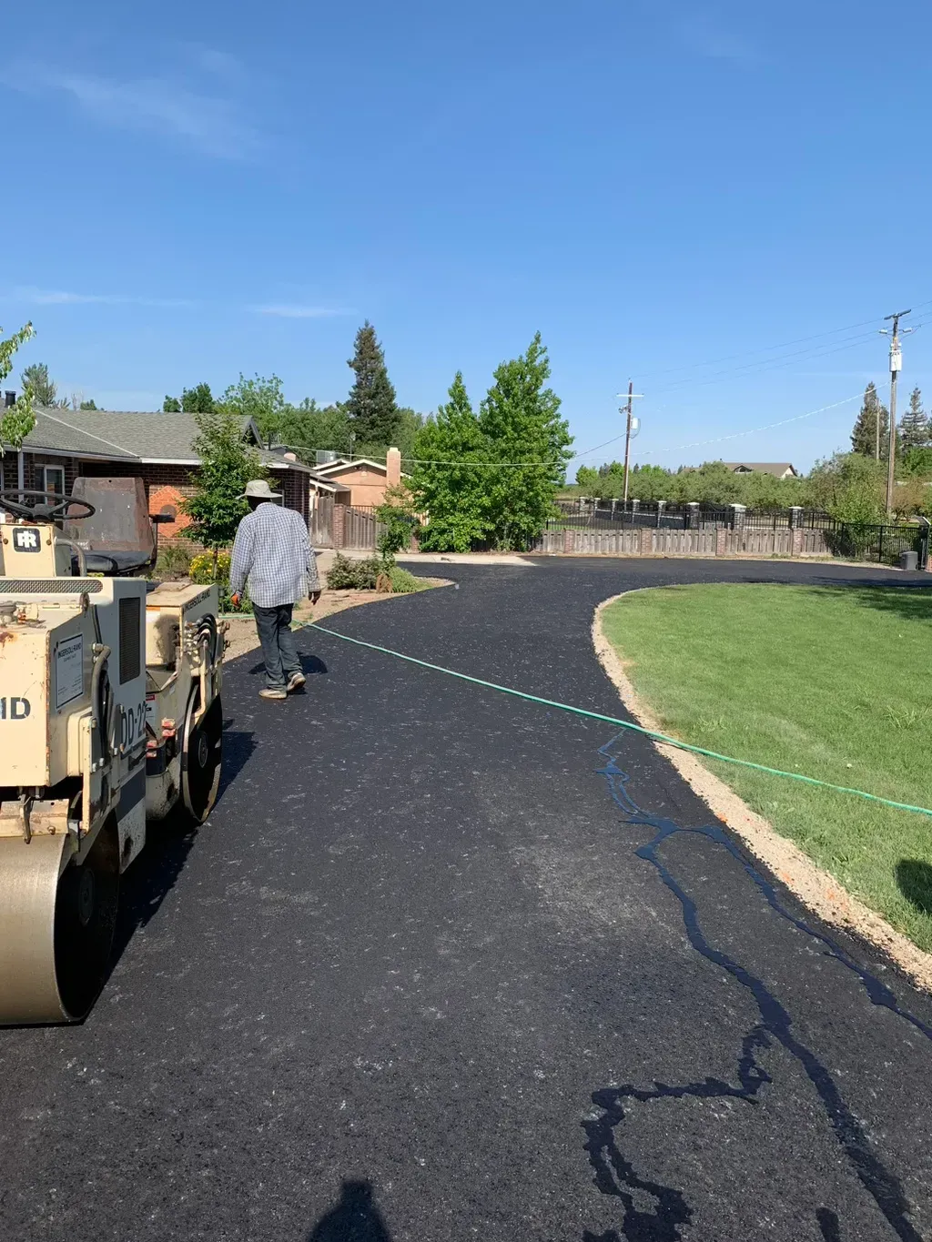Fresh black asphalt being paved along a curved path beside a grassy park on a sunny day