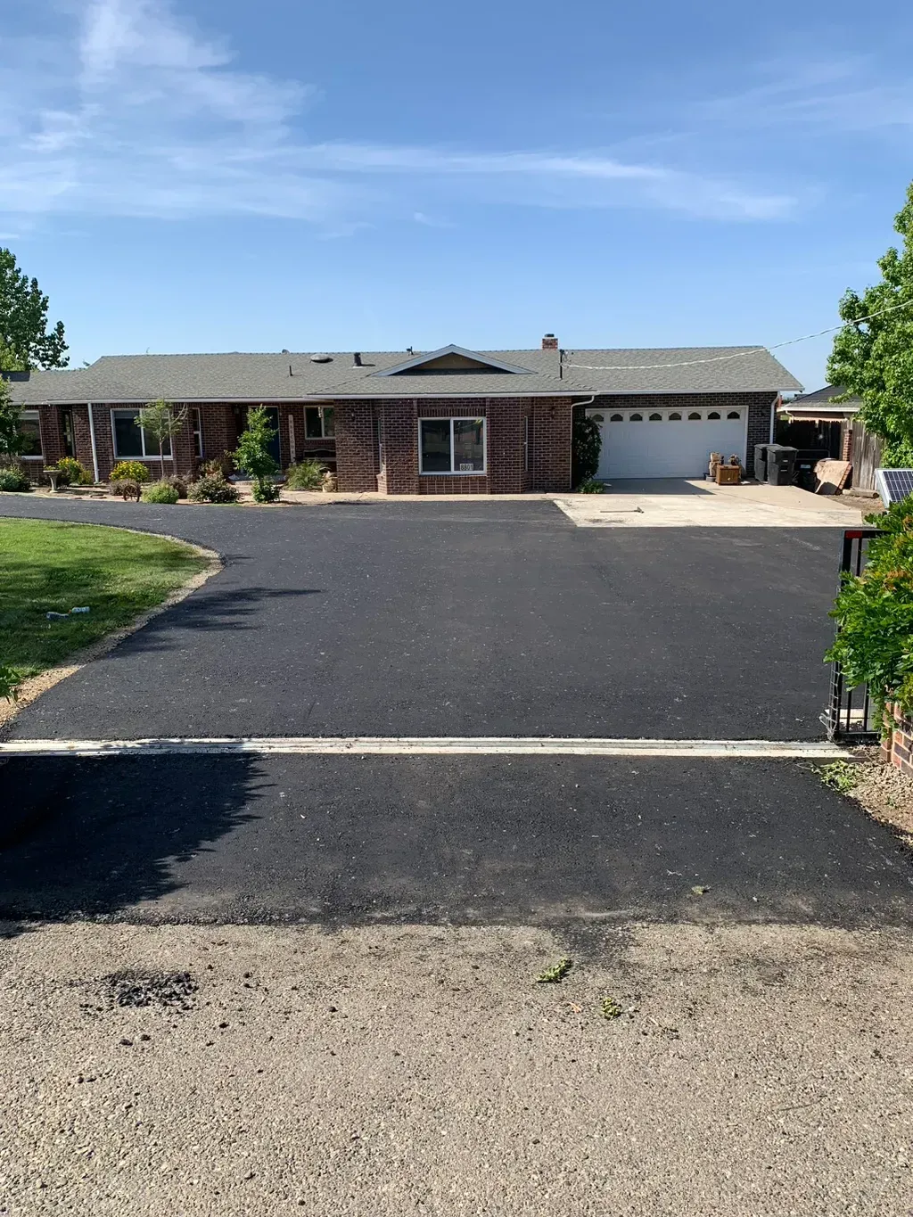 Single-story brick house with a wide blacktop driveway, garage, and a clear blue sky.