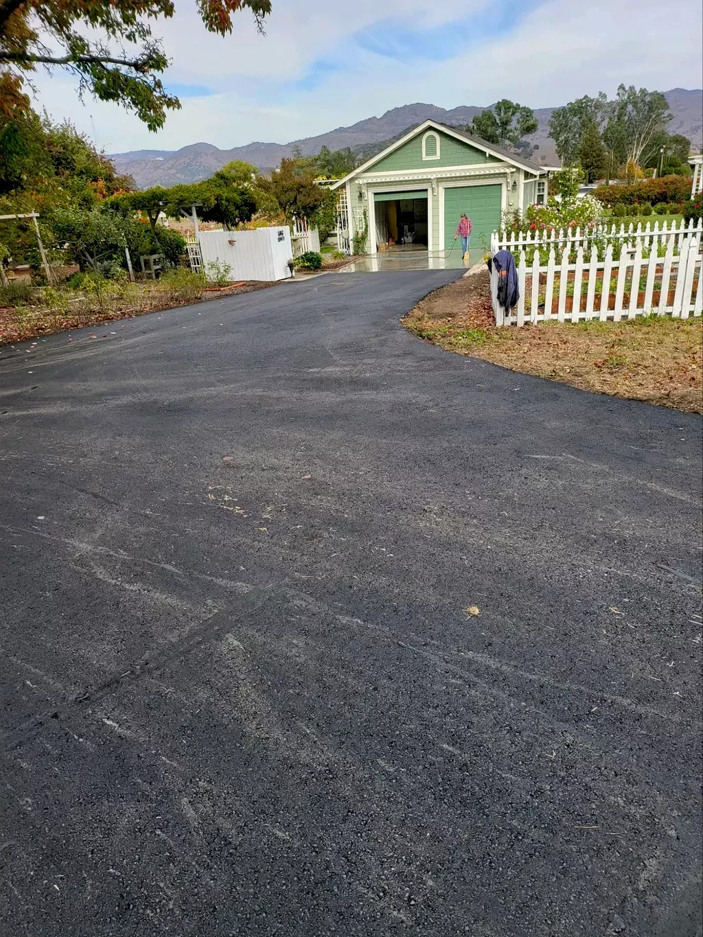 Driveway leading to a mint-green house with a white picket fence and mountains in the background