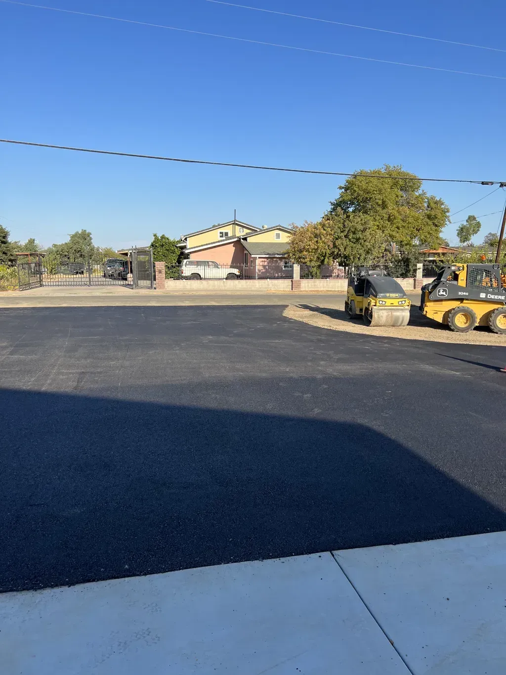 Parking lot under a clear blue sky, with construction equipment near a building and trees in the background.