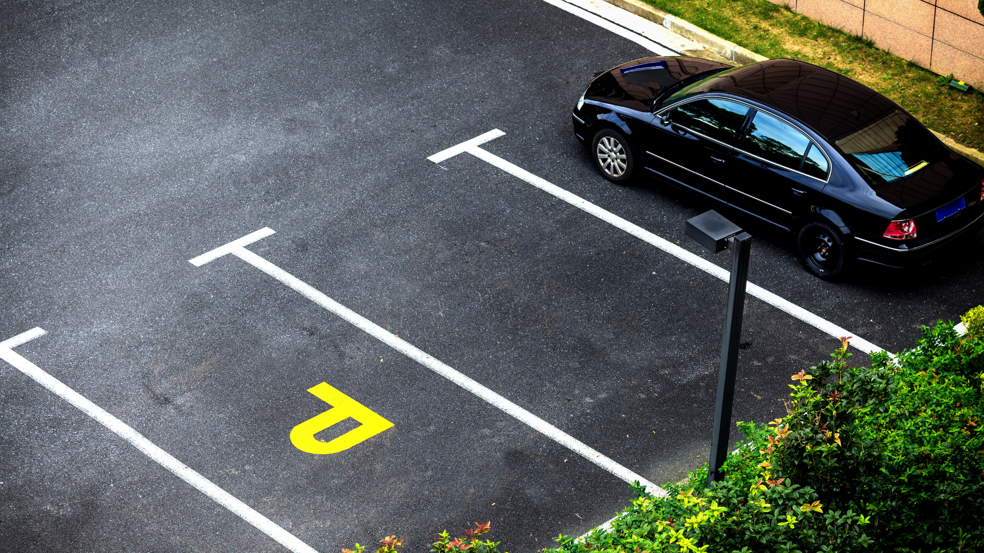 Empty parking lot with white-marked spaces, one black car parked at the top right.