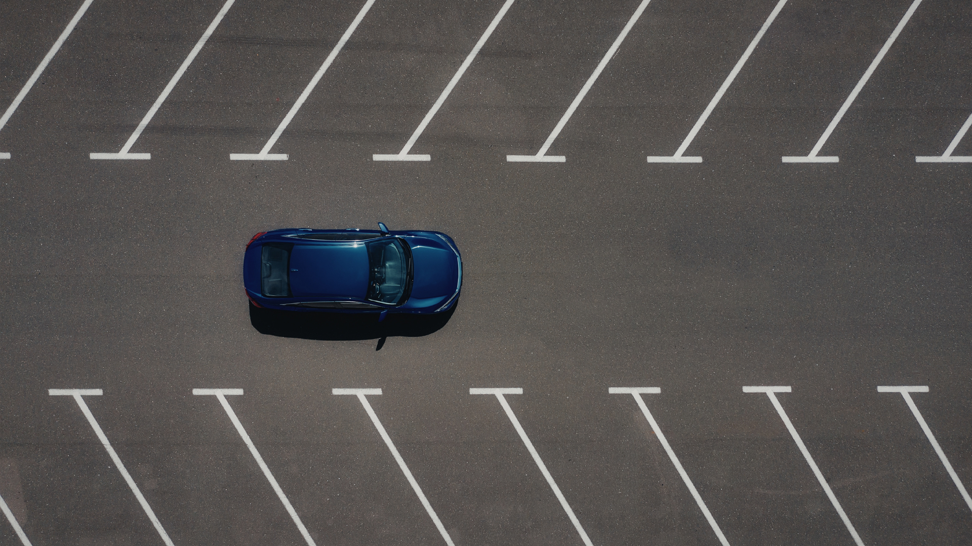 Blue car parked in a nearly empty parking lot with white painted spaces