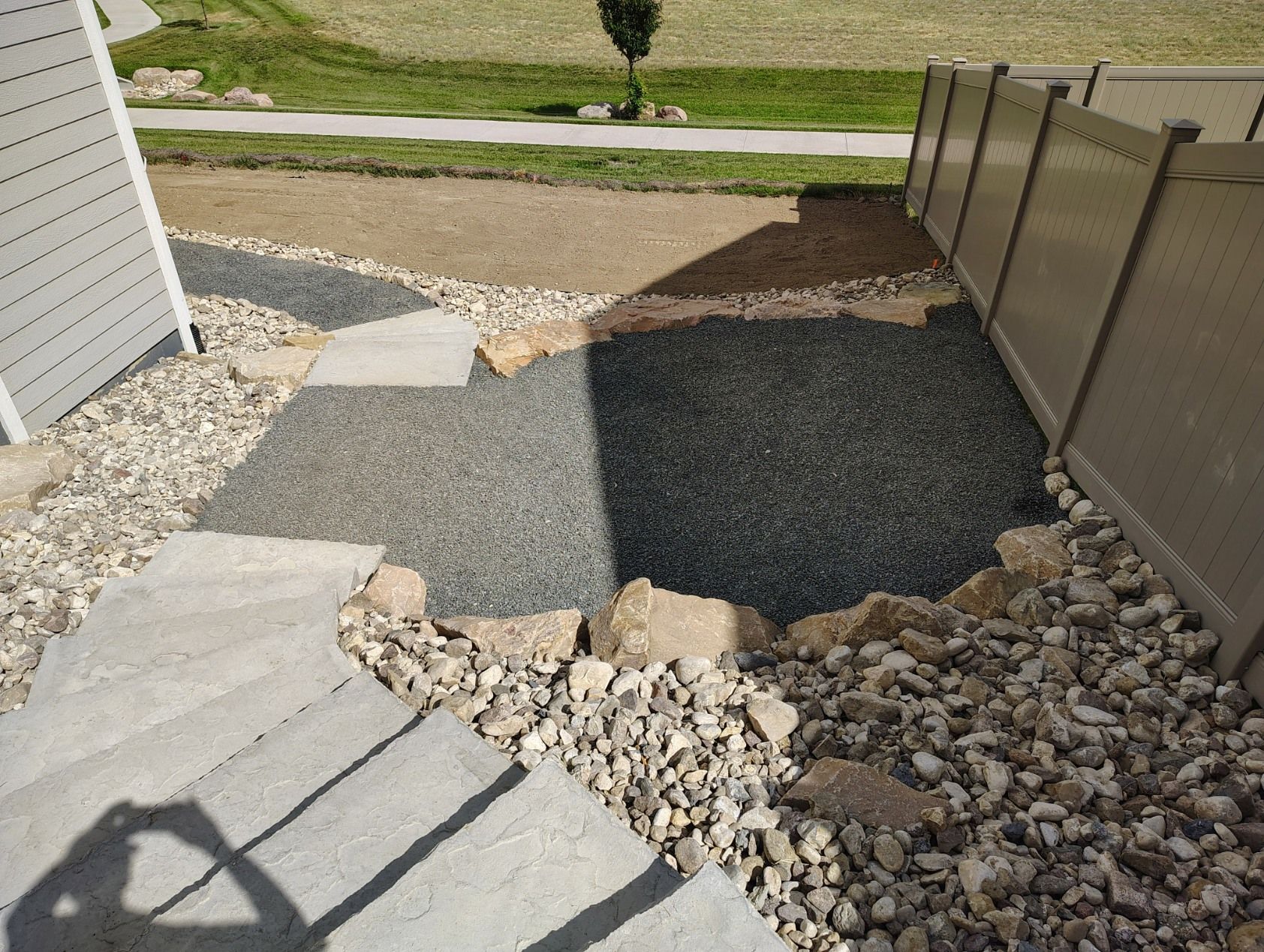Concrete steps lead down to a transition area with grey gravel, beige rocks, and a tan privacy fence outdoors.