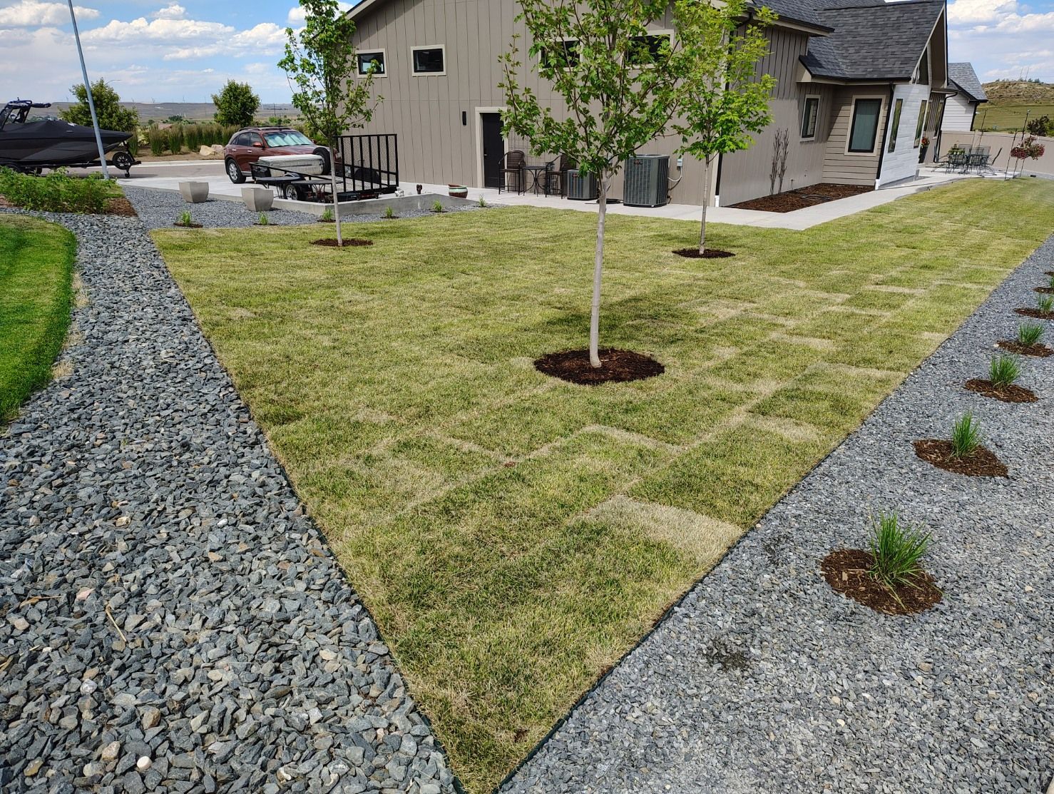 A newly installed grass lawn bordered by gray gravel paths and a house in the background under a blue sky.