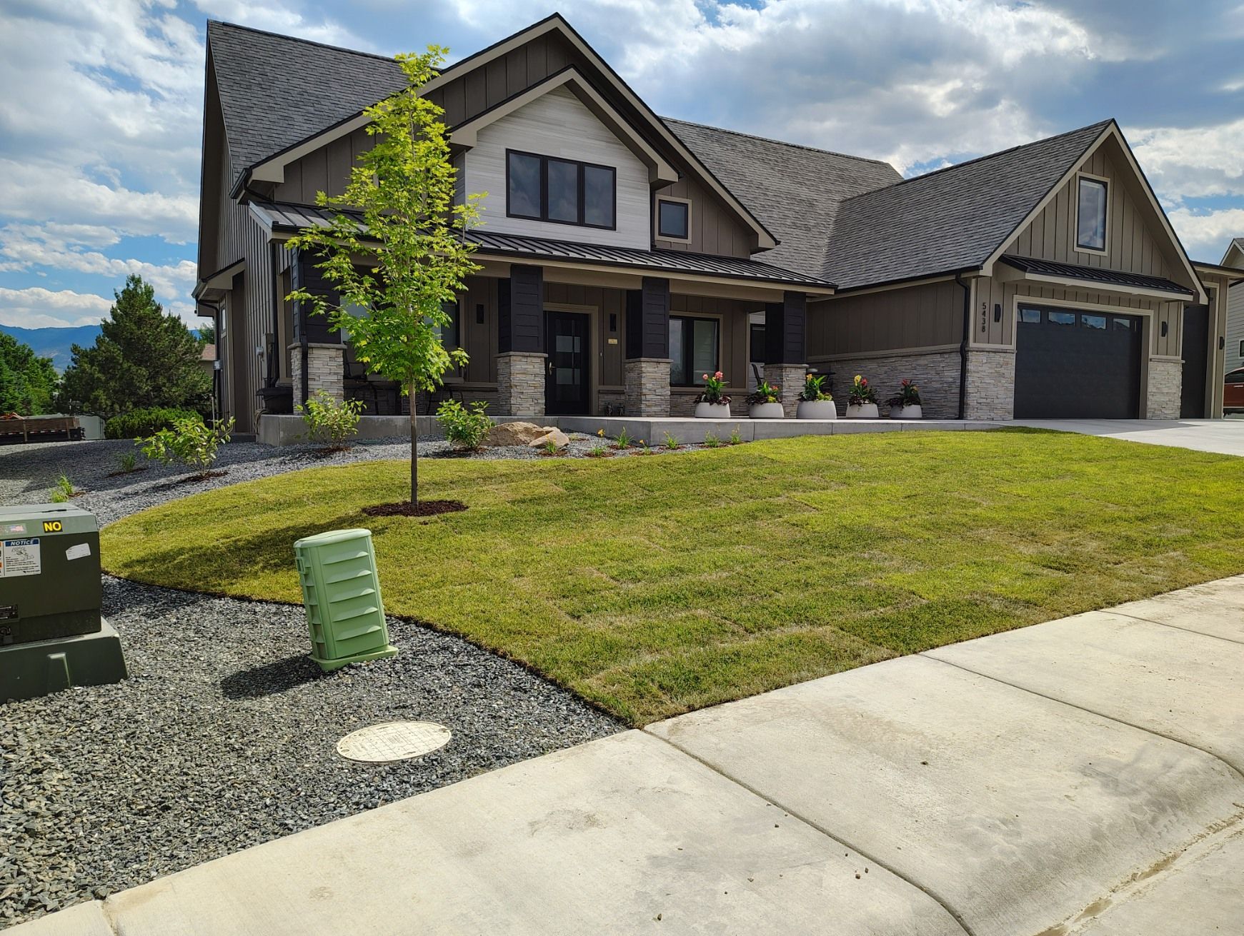 A two-story suburban house with stone and brown siding, a dark roof, a front porch, and a landscaped lawn.