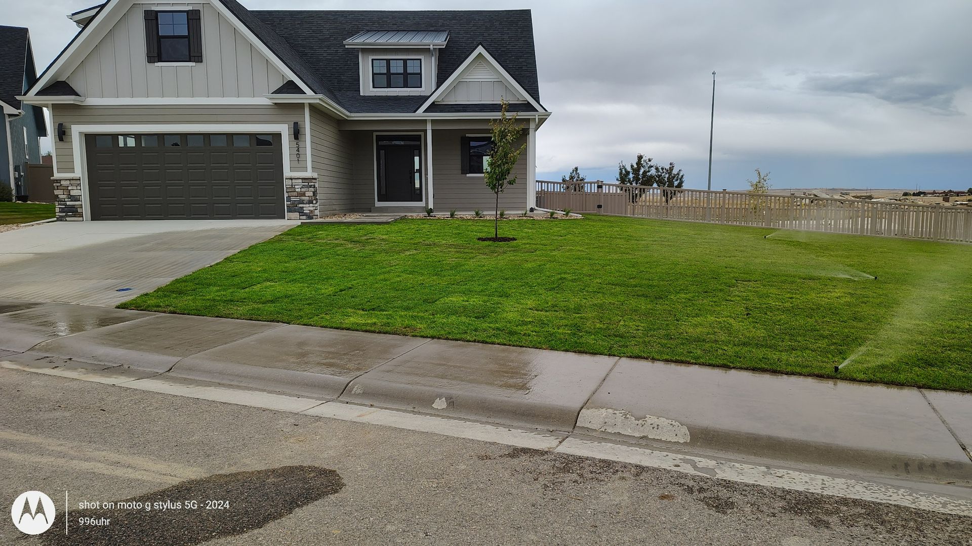 A single-story suburban house with a gray garage, tan siding, and a freshly planted front lawn under a cloudy sky.