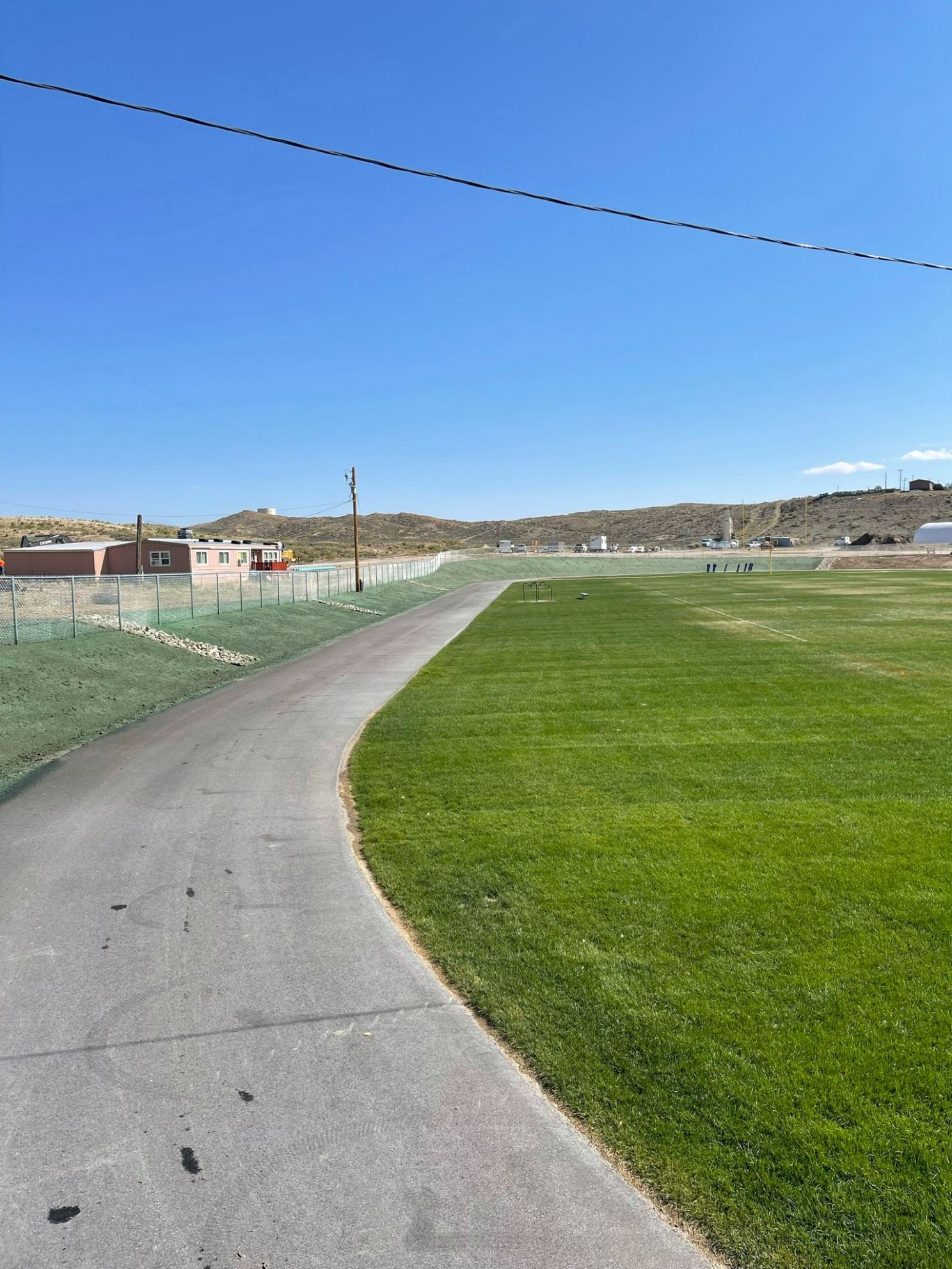 A paved path curves beside a wide, bright green lawn under a clear blue sky, with desert hills in the background.
