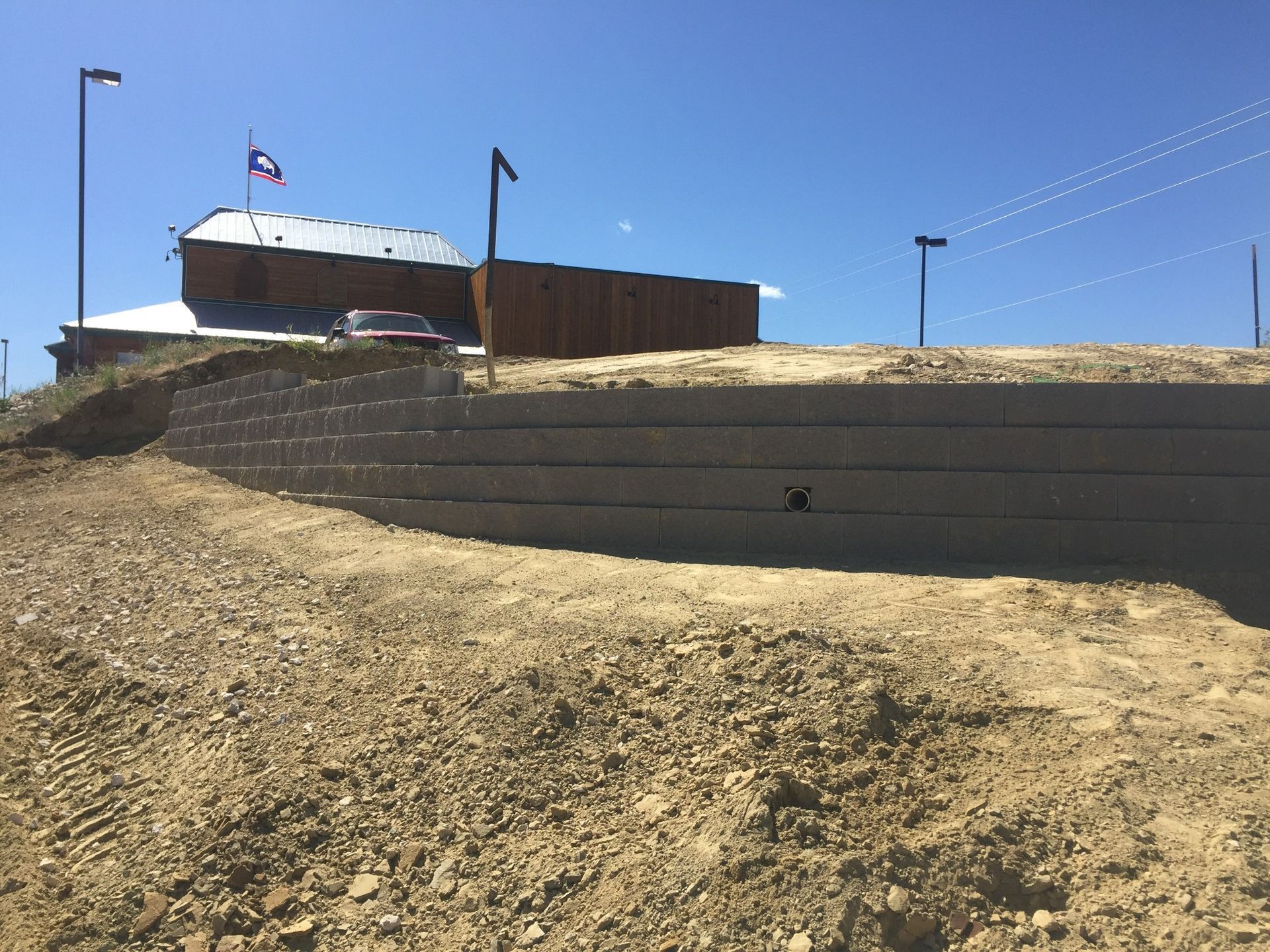 A light-colored segmental retaining wall curves across a dirt construction site under a clear blue sky.