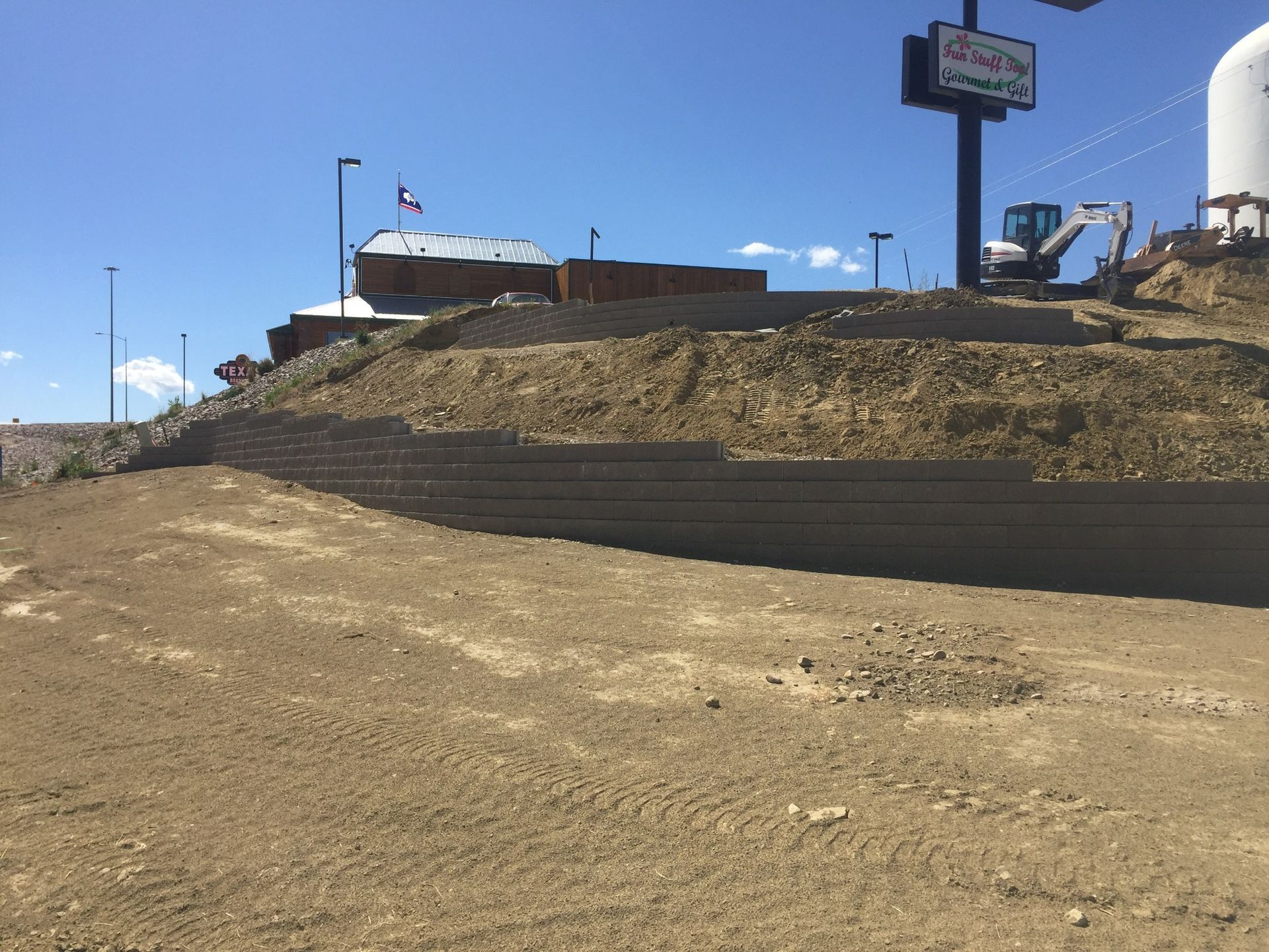 A multi-tiered retaining wall under construction in a dirt lot beneath a bright blue sky.