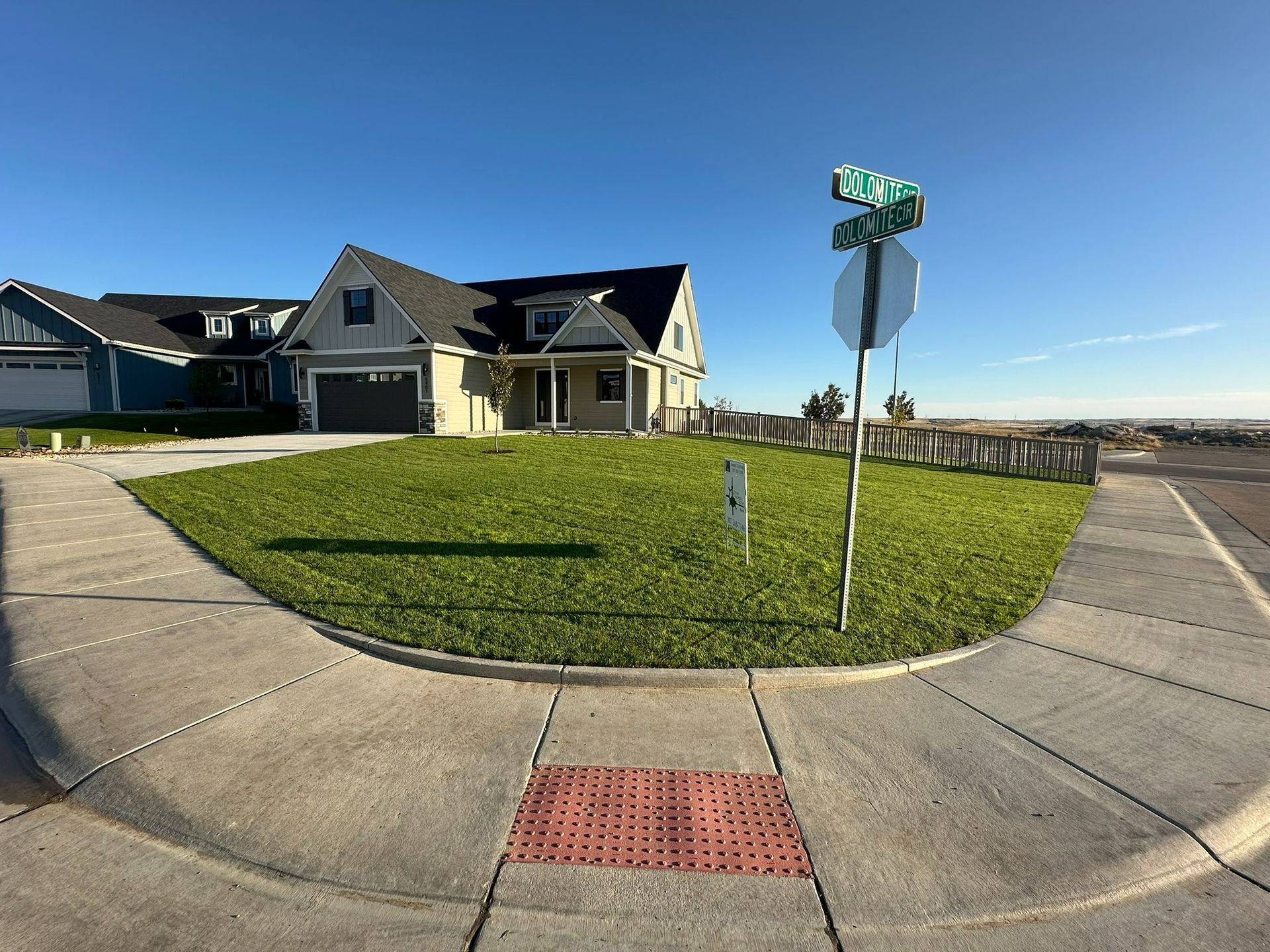 A street corner with a grassy yard, a house, and a street sign on a clear, sunny day.