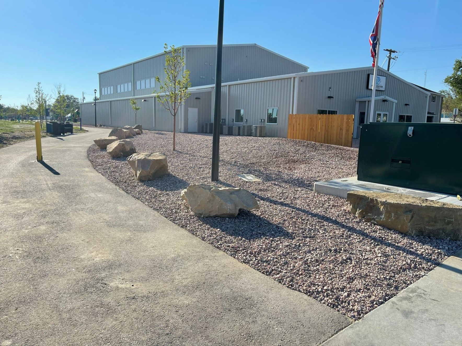 A grey metal building with a gravel landscaping area, large rocks, and a paved path under a clear blue sky.
