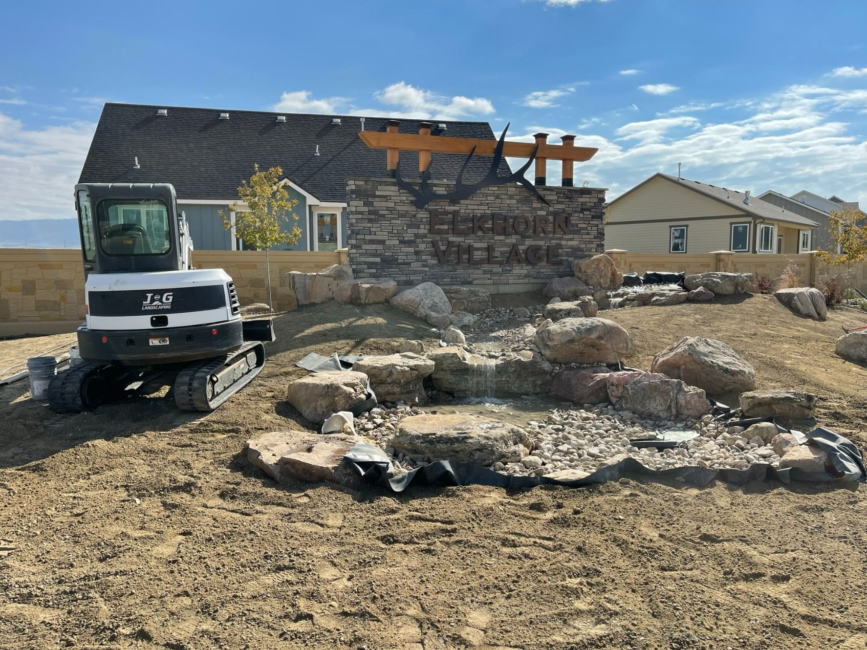 A white construction excavator sits next to a stone neighborhood entrance sign for 