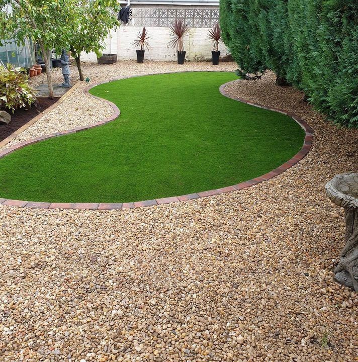 Landscaped backyard with a bright green lawn island surrounded by gravel and shrubs