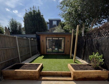 Backyard with artificial grass, raised wooden planters, and a small modern shed at the end.