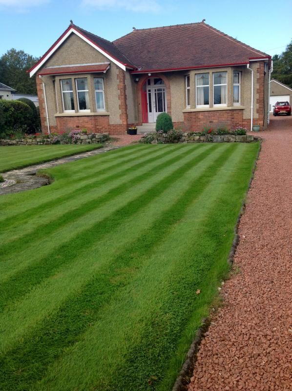 Single-story brick house with a striped green lawn and gravel driveway