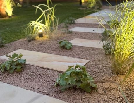 Illuminated stepping stones through a gravel garden with small green plants at dusk