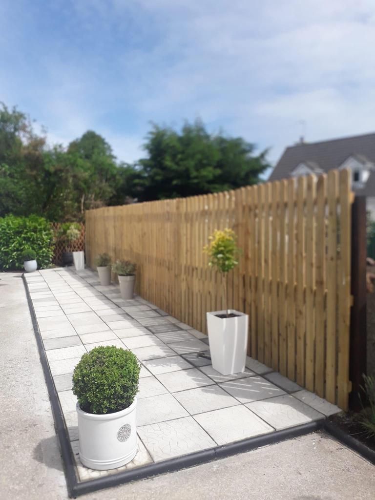 Sunny patio with white pavers, potted plants, and a wooden fence along the side yard