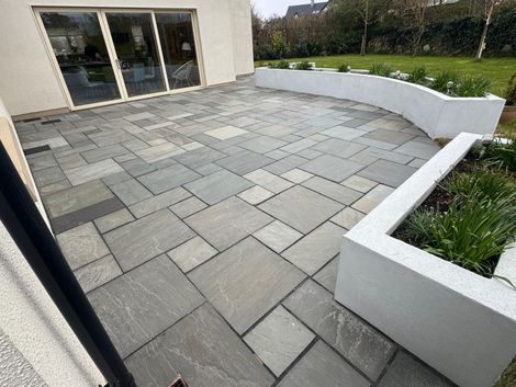 Modern patio with gray stone pavers, white retaining walls, and glass doors beside a garden.