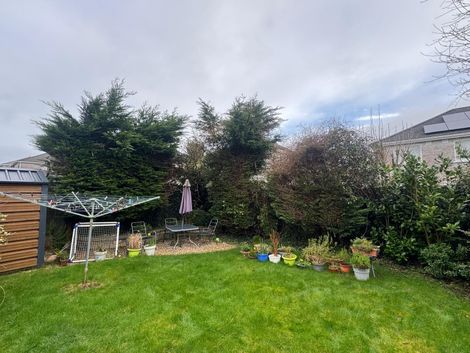 Backyard lawn with trees, flower beds, a patio umbrella, and a clothesline under a cloudy sky