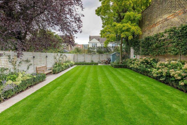 Manicured backyard lawn with flower beds, stone walls, and tall trees