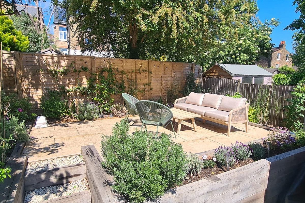 Backyard patio with wicker sofa, green chair, and plants in a sunny garden