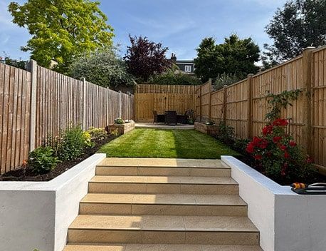 Garden steps leading to a manicured lawn, bordered by wooden fences and flower beds under a clear sky