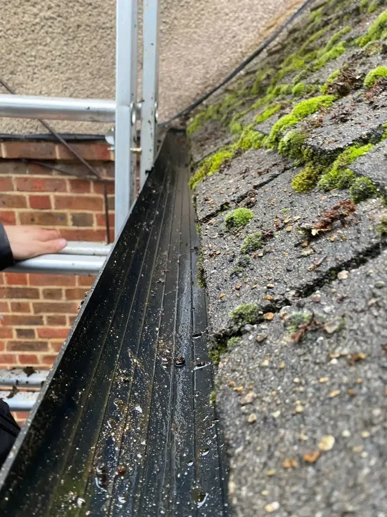Roof gutter clogged with debris beside a wall and scaffolding pole