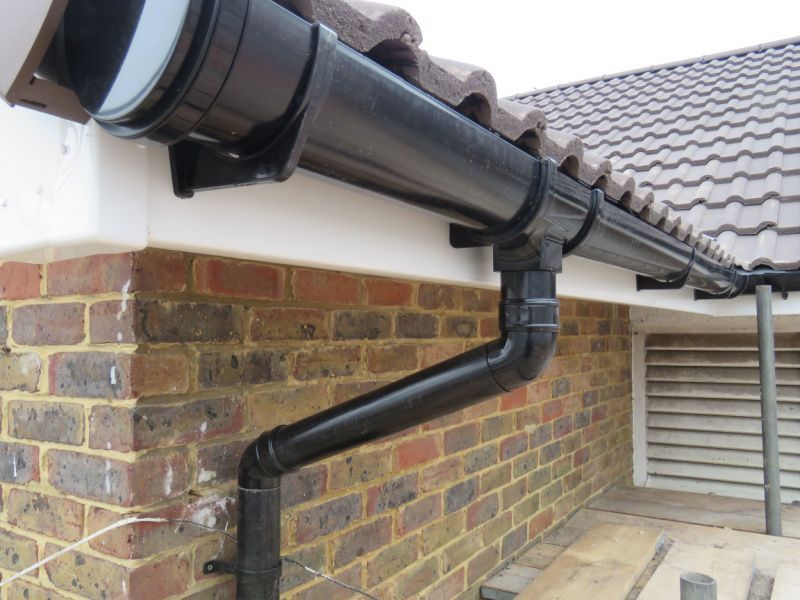 Black rain gutter and downspout on a brick house exterior with a tiled roof