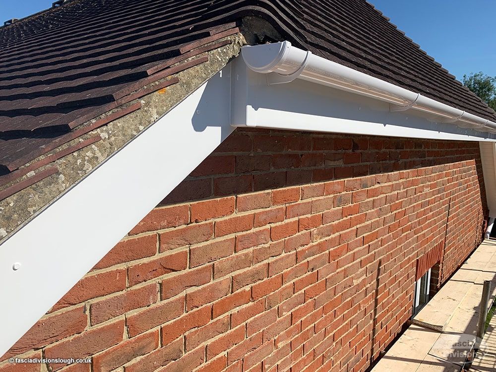 Brick house gable with white trim, dark roof tiles, and red brick wall in sunlight